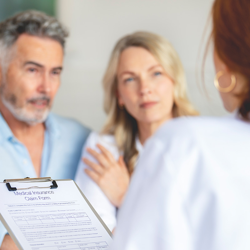Doctor filling out medical insurance form with mature couple